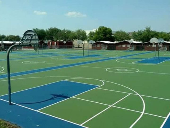 Outdoor basketball courts with blue-painted key areas and several hoops under a clear sky.