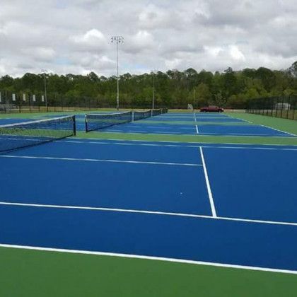 Empty outdoor tennis courts with blue and green surfaces under a cloudy sky.