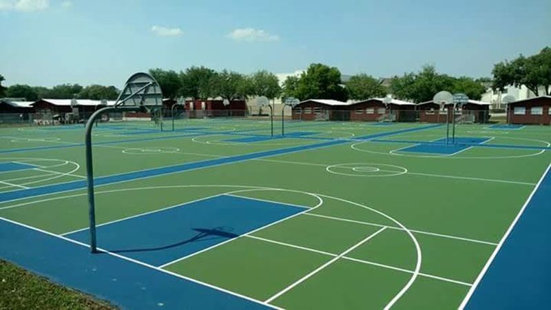 Outdoor sports court with green and blue surfaces, white lines, and hoops under a clear sky.
