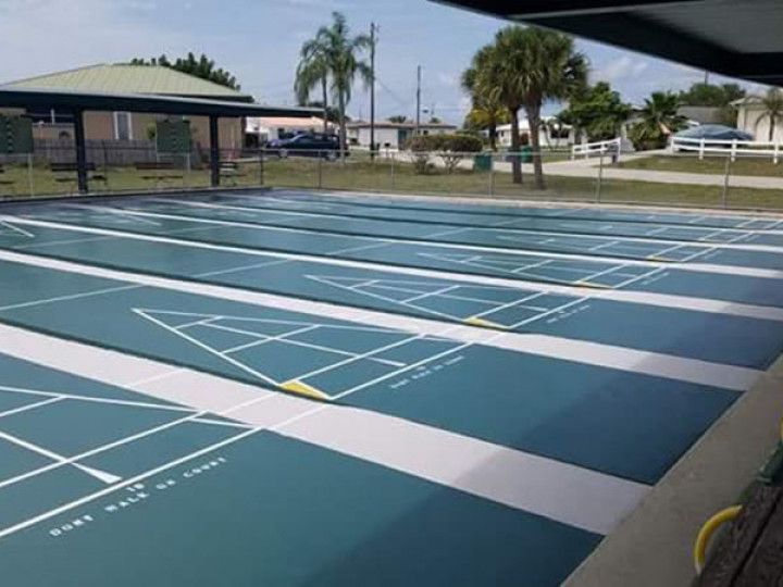Empty blue outdoor sports courts with white lines beside a covered pavilion and palm trees