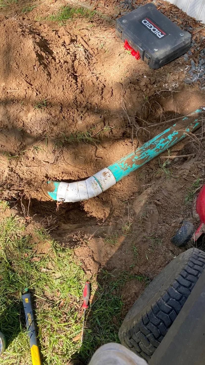 A person is digging a hole in the ground to install a pipe.