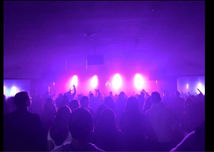 Crowded concert hall with purple stage lights and silhouetted audience members
