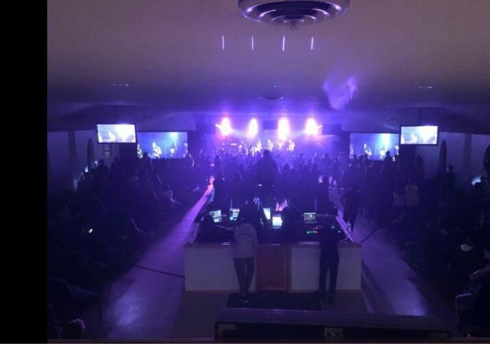 Dark concert hall with purple stage lights and a crowd facing the stage
