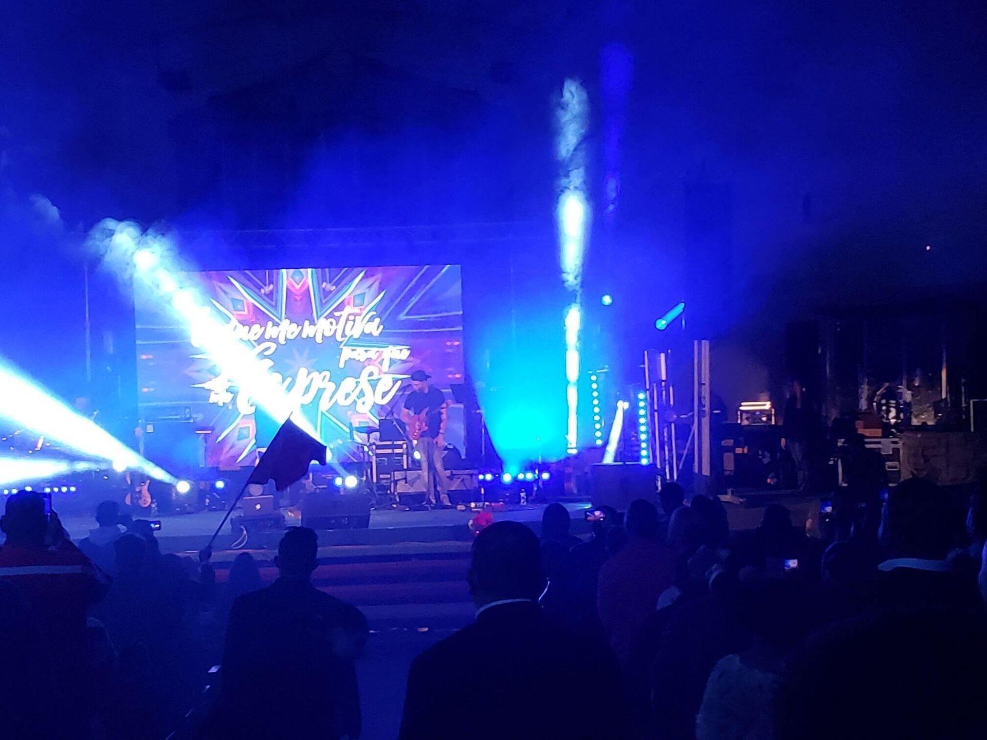 Concert stage with blue lights, a singer performing, and an audience in silhouette
