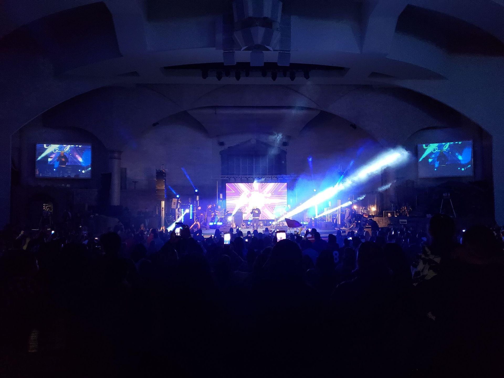 Concert stage in a dark auditorium with bright blue lights and a crowd in silhouette