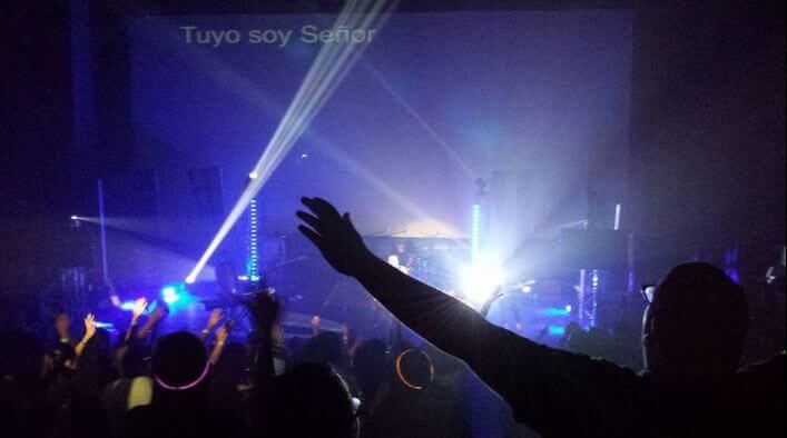 Concert crowd with raised hands and bright blue-purple stage lights