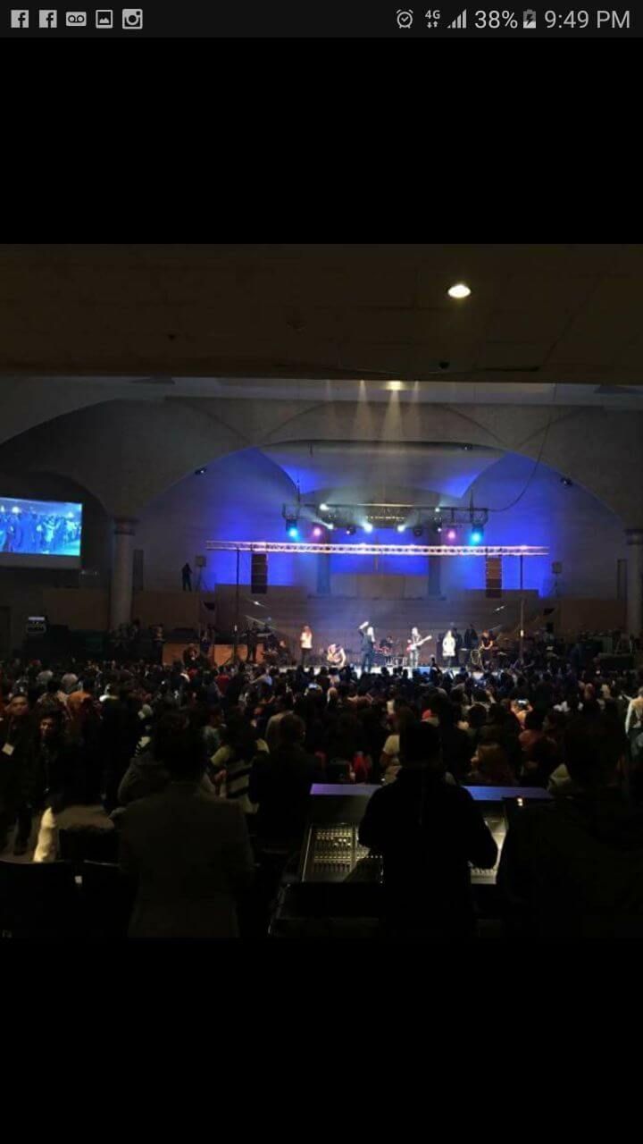 Concert stage with blue lights and a large crowd gathered indoors at night