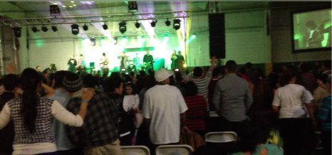 Crowded indoor concert with audience facing a green-lit stage