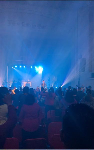Crowd watching a blue-lit concert stage in a large indoor venue
