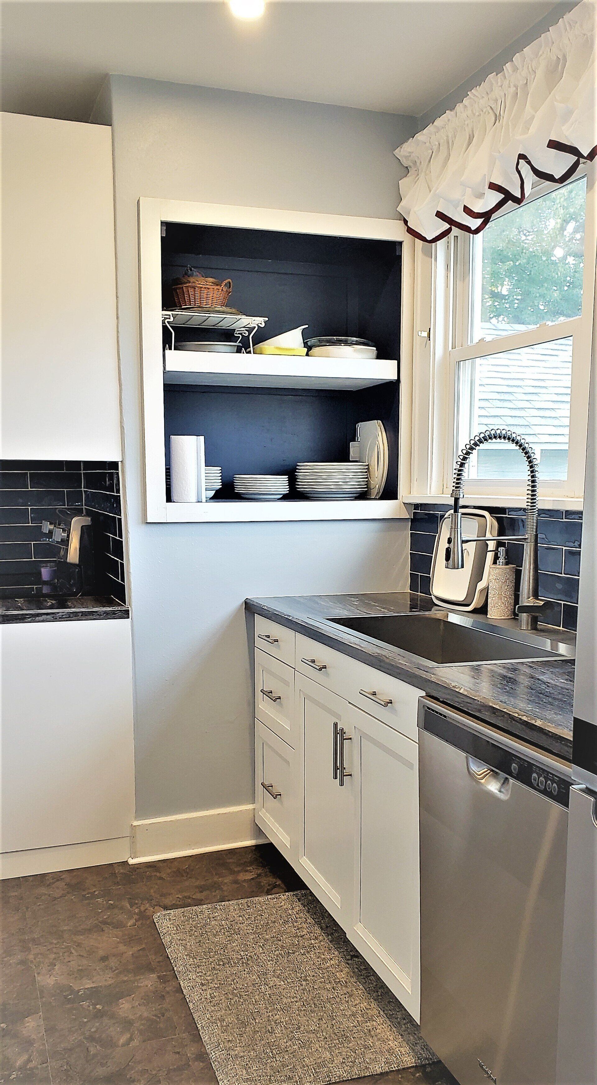 Kitchen with white cabinets, built-in shelves, stainless steel appliances, and a window with curtains.