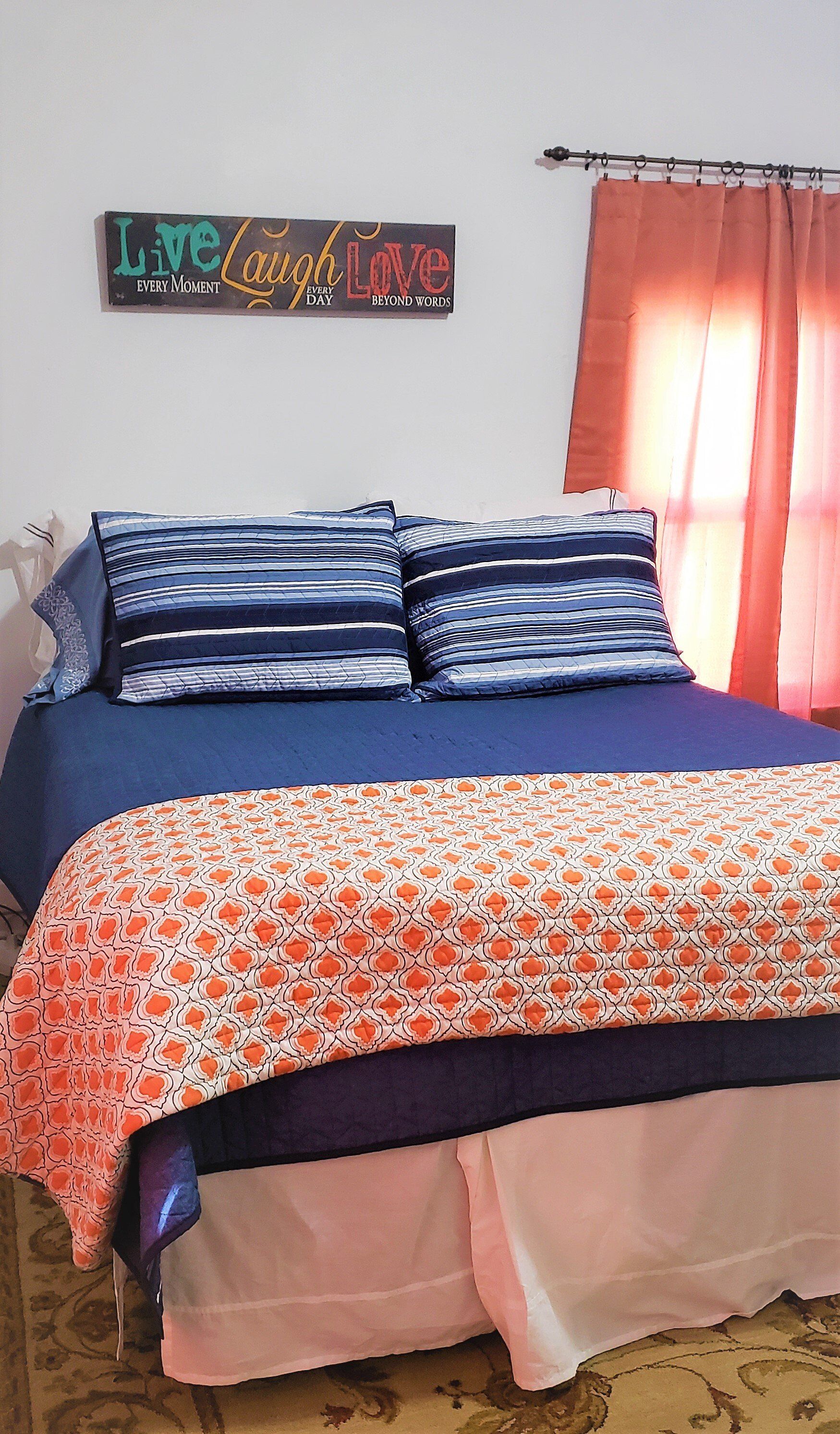 Bed with navy blue bedding, floral throw, and peach curtains. 