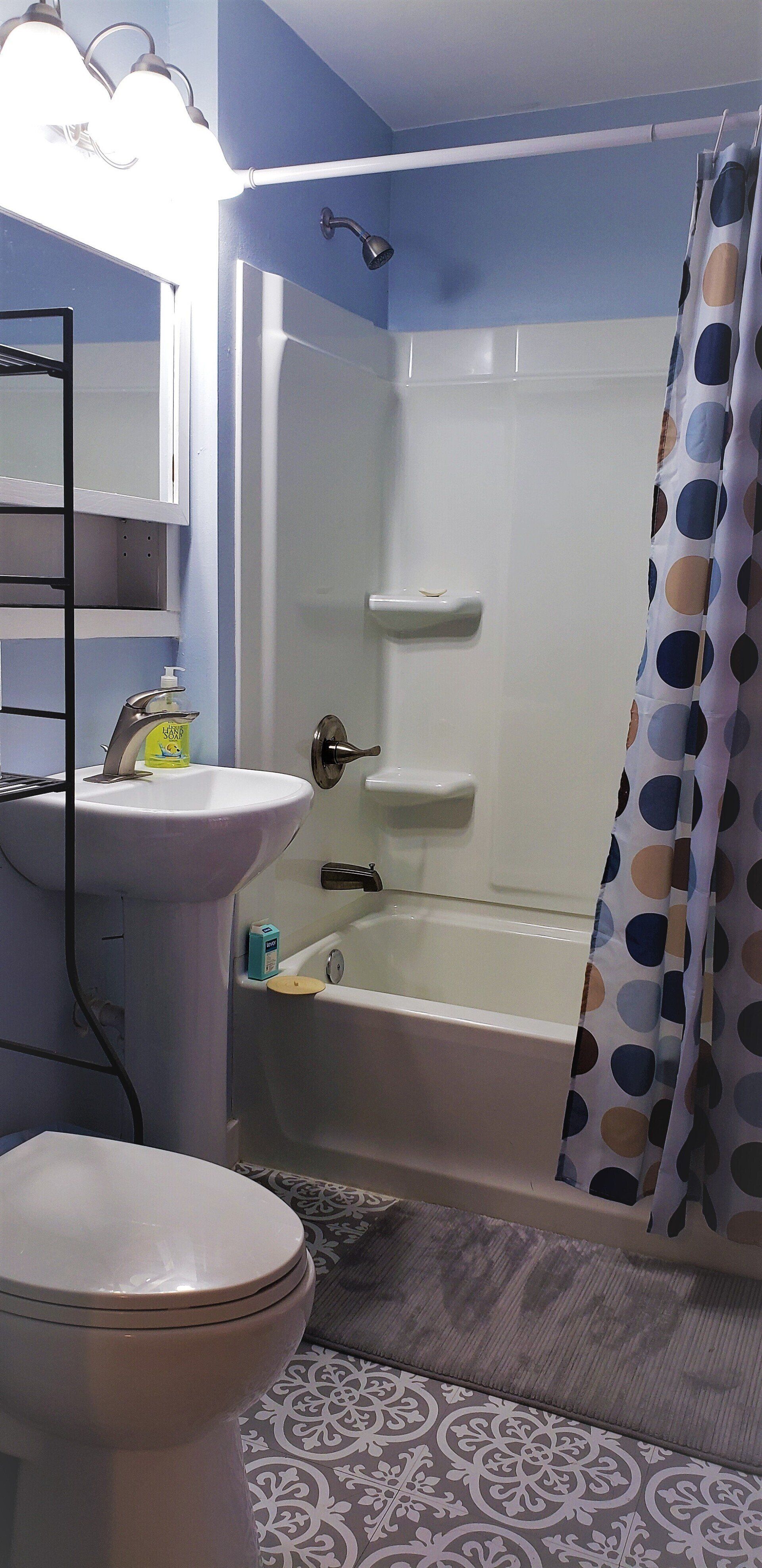 Bathroom with white fixtures, blue walls, patterned shower curtain and gray patterned rug.