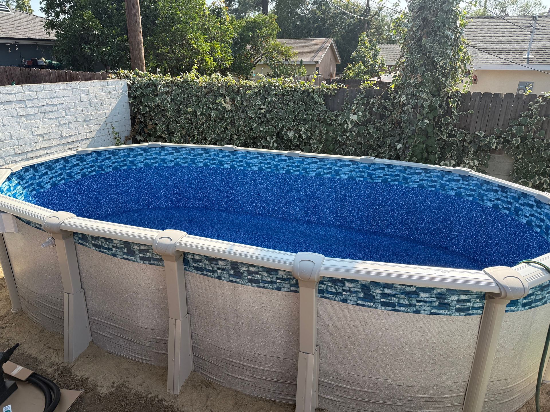 Above-ground backyard pool with blue water and white frame beside a hedge and wall