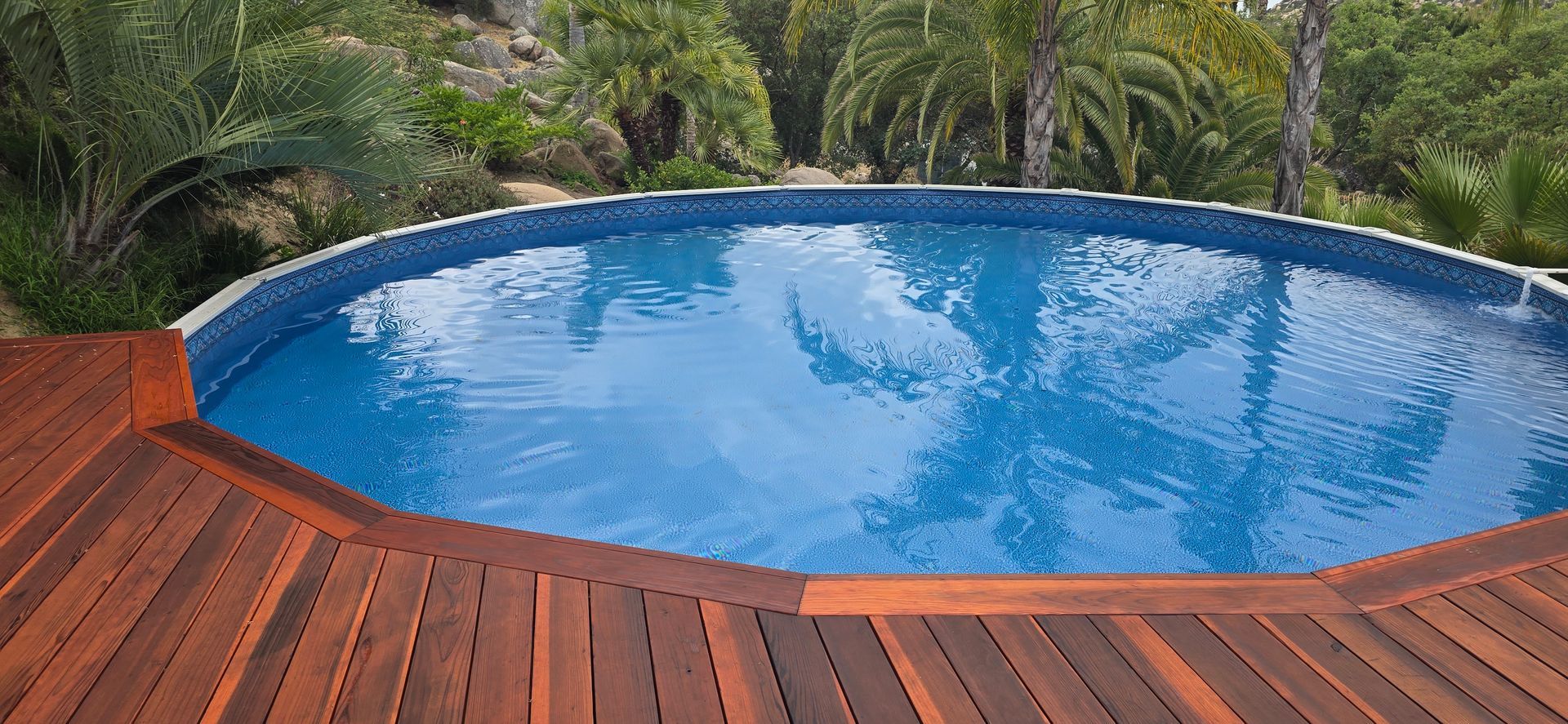 Round blue pool beside a wooden deck, surrounded by tropical greenery