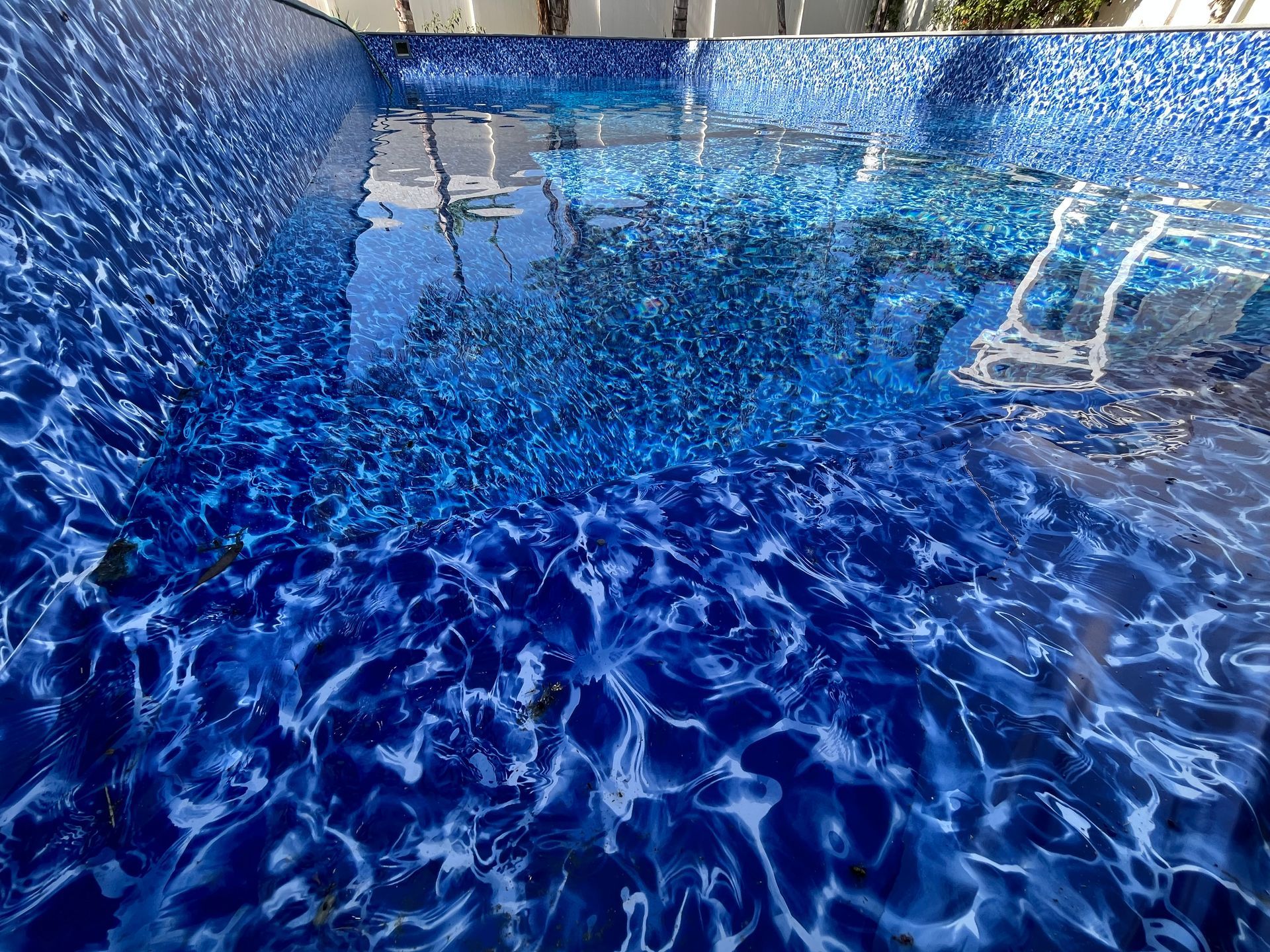 Blue water splashing in a swimming pool, with sunlight shimmering across the surface.