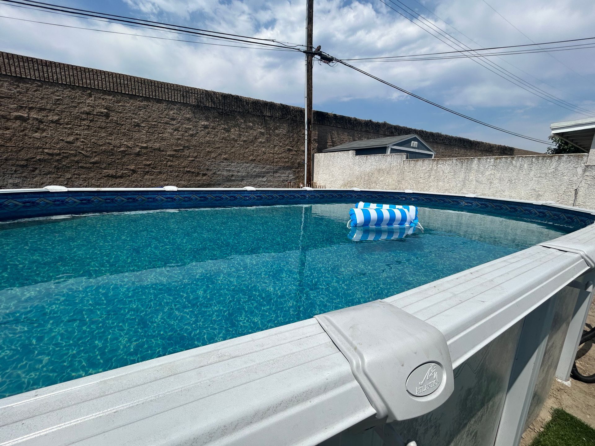 Above-ground pool with blue water and a floating blue-and-white ball under a bright sky
