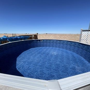 Empty above-ground pool with blue liner in a sunny backyard under a clear sky