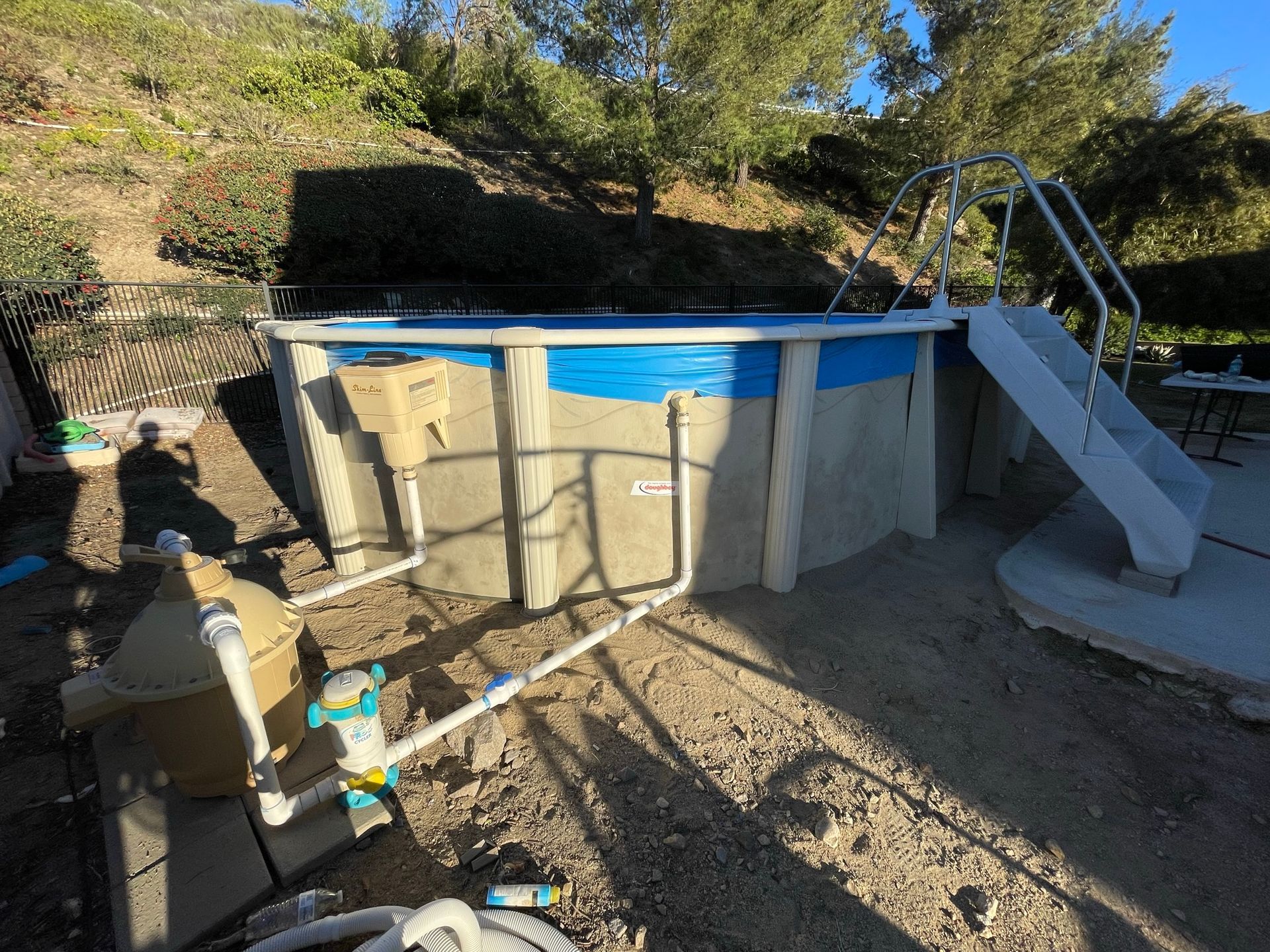 Above-ground pool with blue interior, beige supports, and a white slide in a backyard.