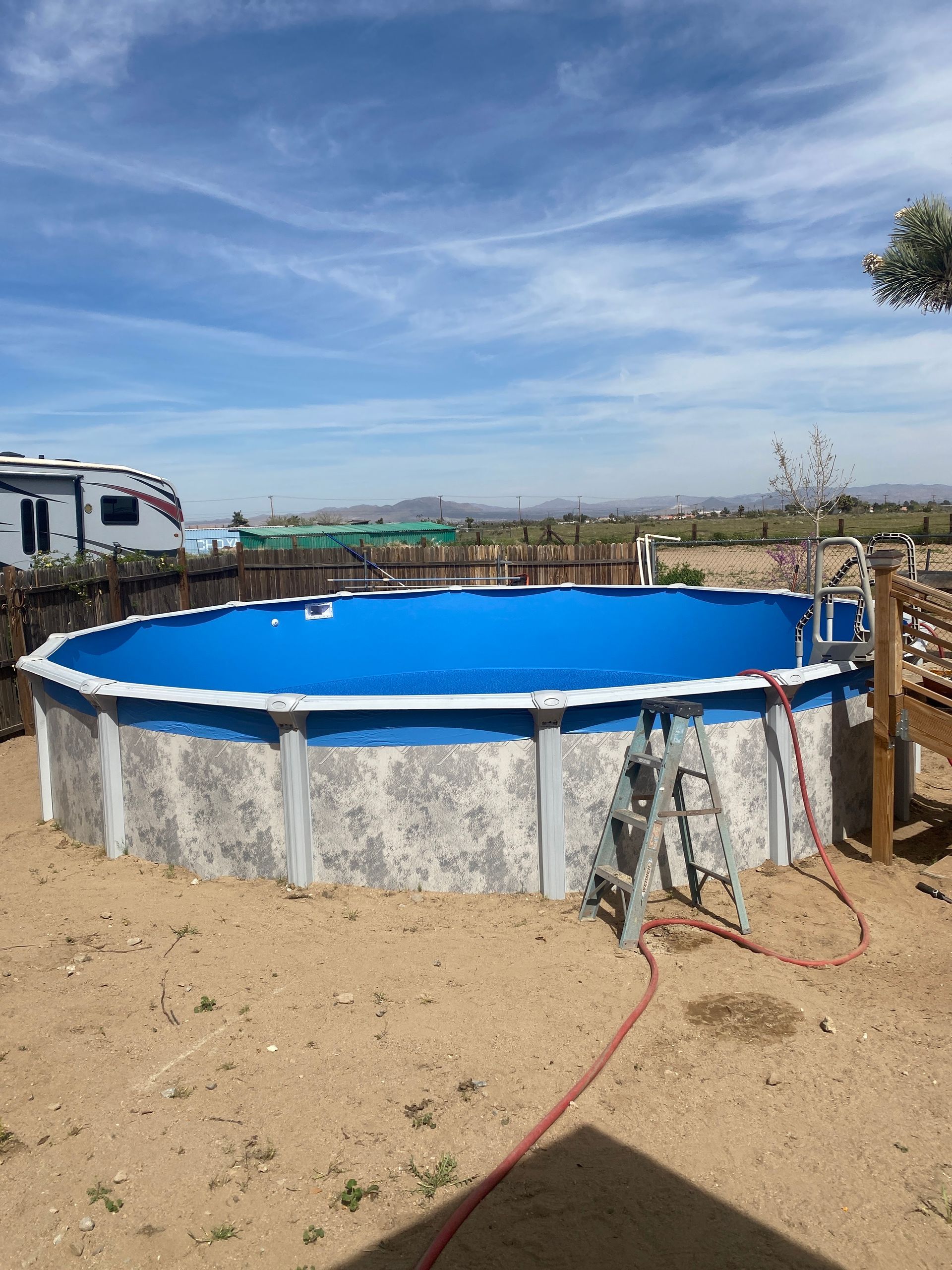 Round above-ground pool with bright blue water in a dry, open yard under a cloudy sky