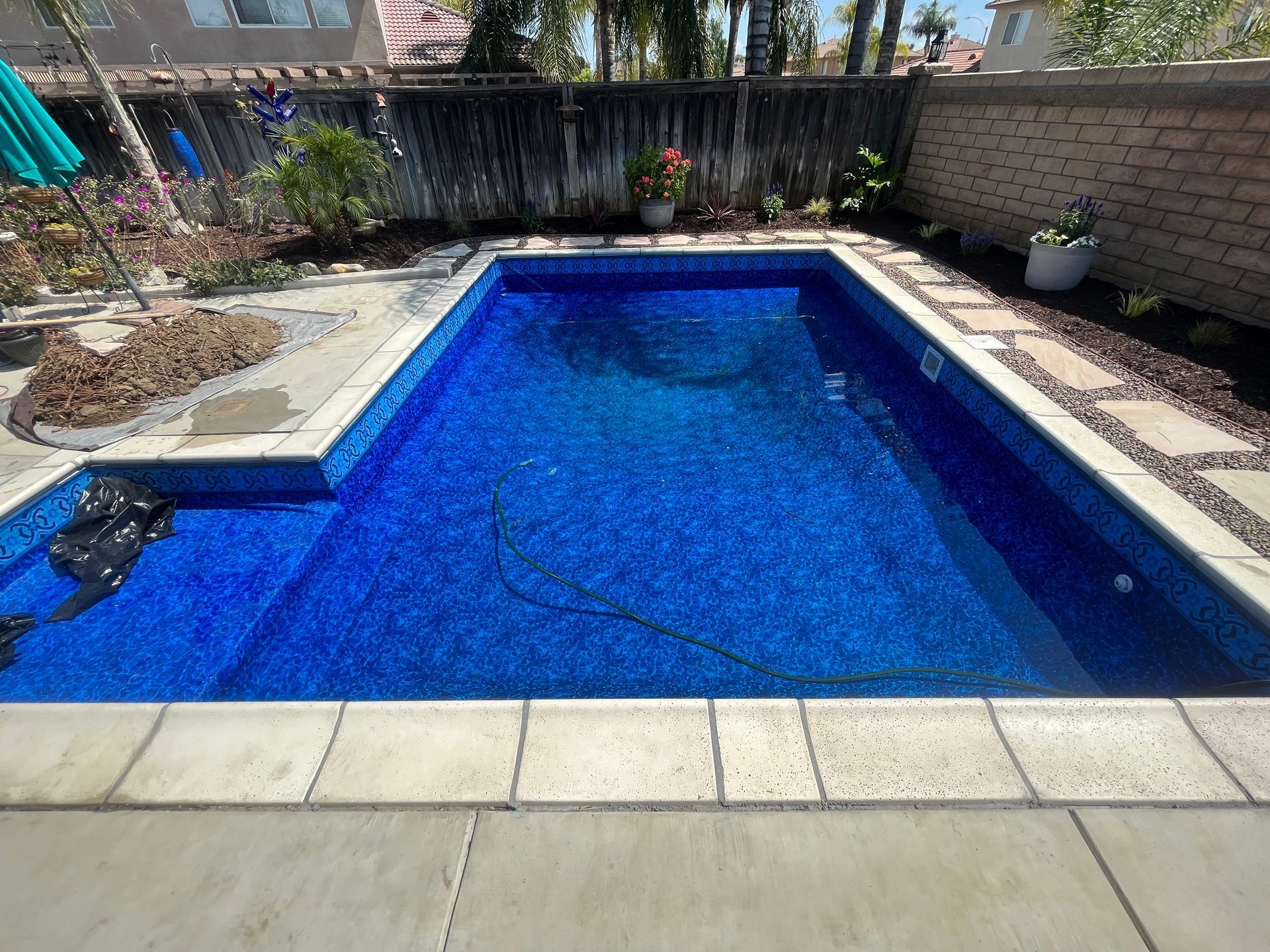 Backyard swimming pool with bright blue water, stone deck, and potted plants along the fence