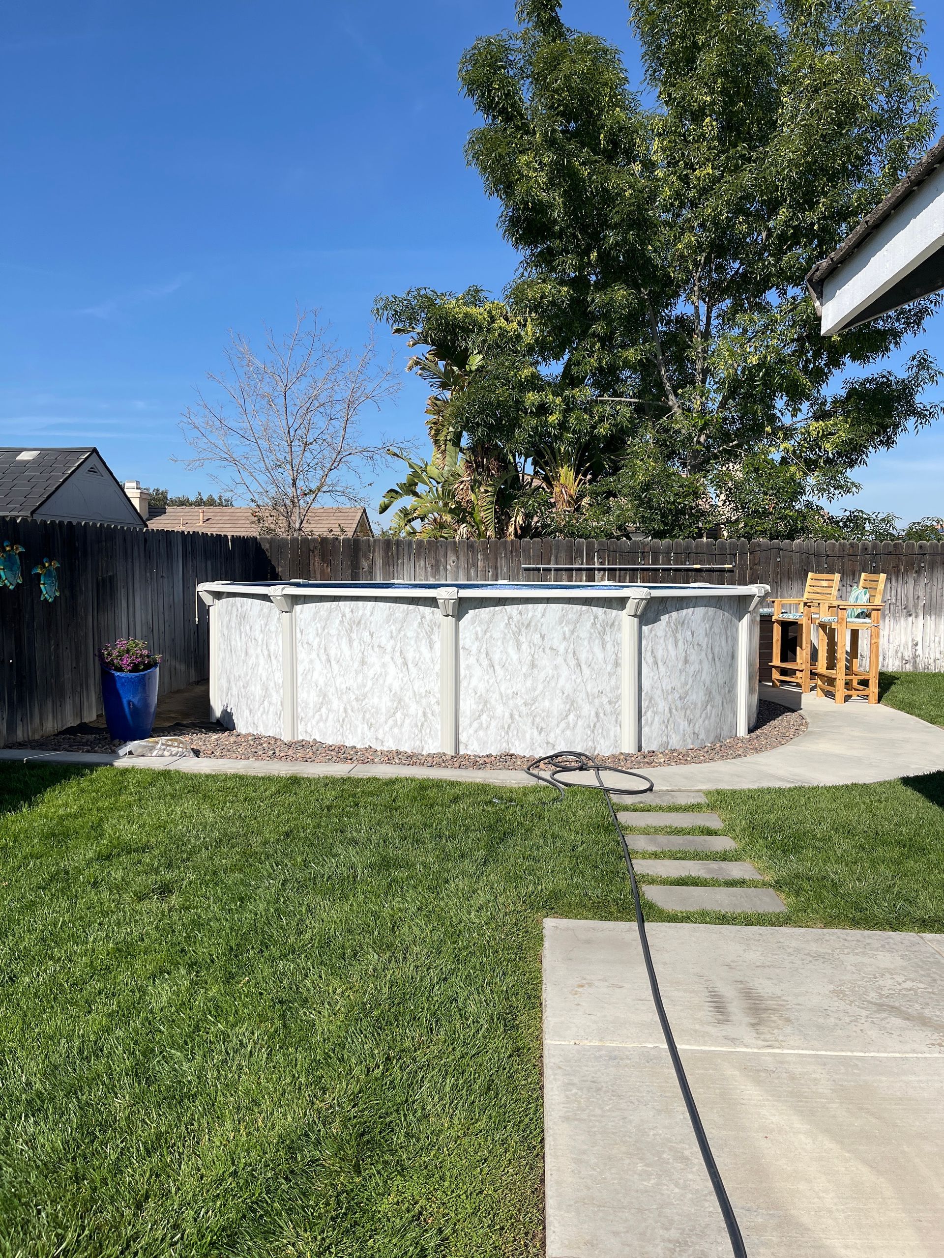 Backyard with a round above-ground pool, green lawn, concrete patio, and a tree under a blue sky