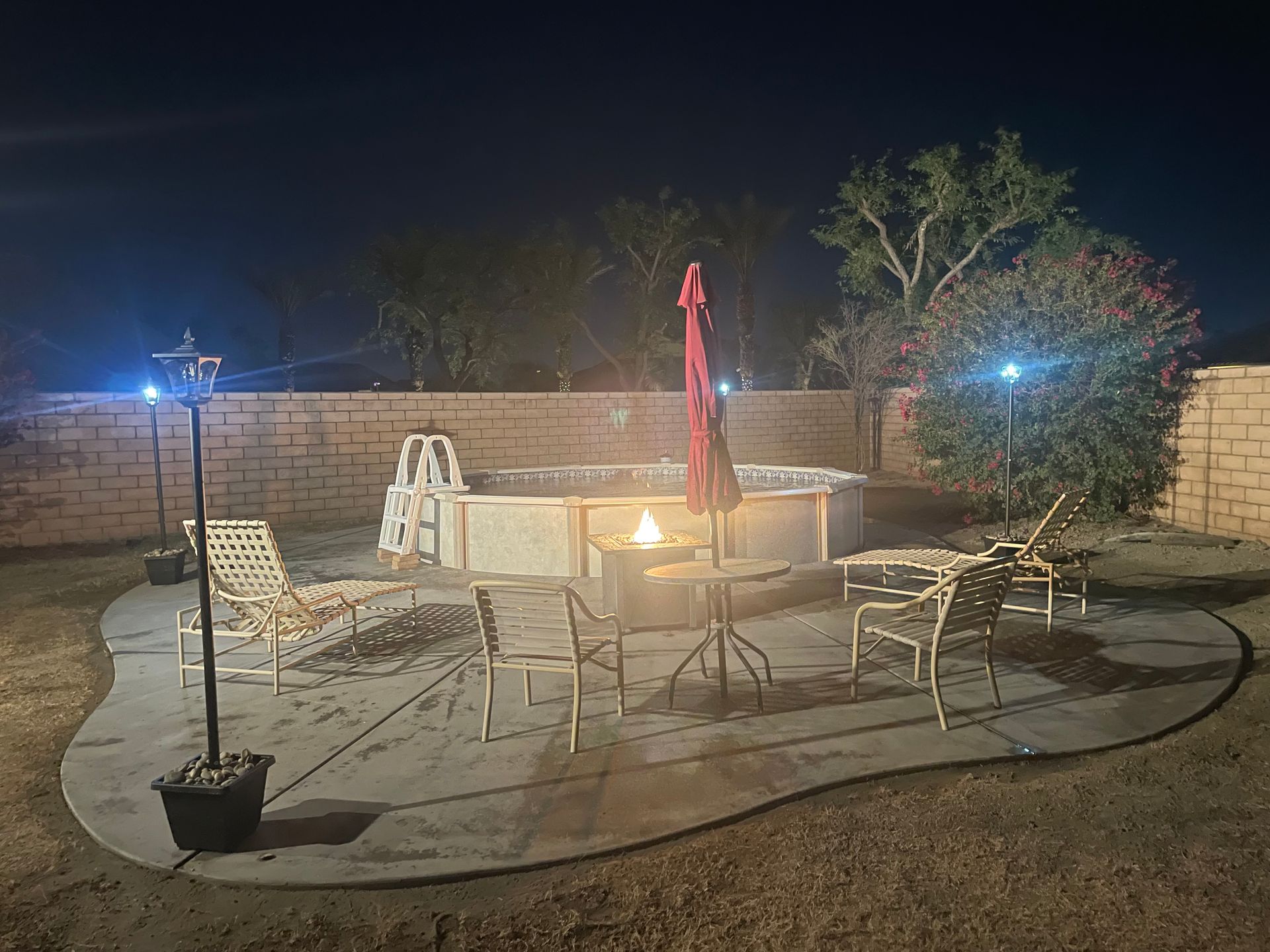 Nighttime patio with chairs, table, fire pit, blue lights, and a stone wall in the background