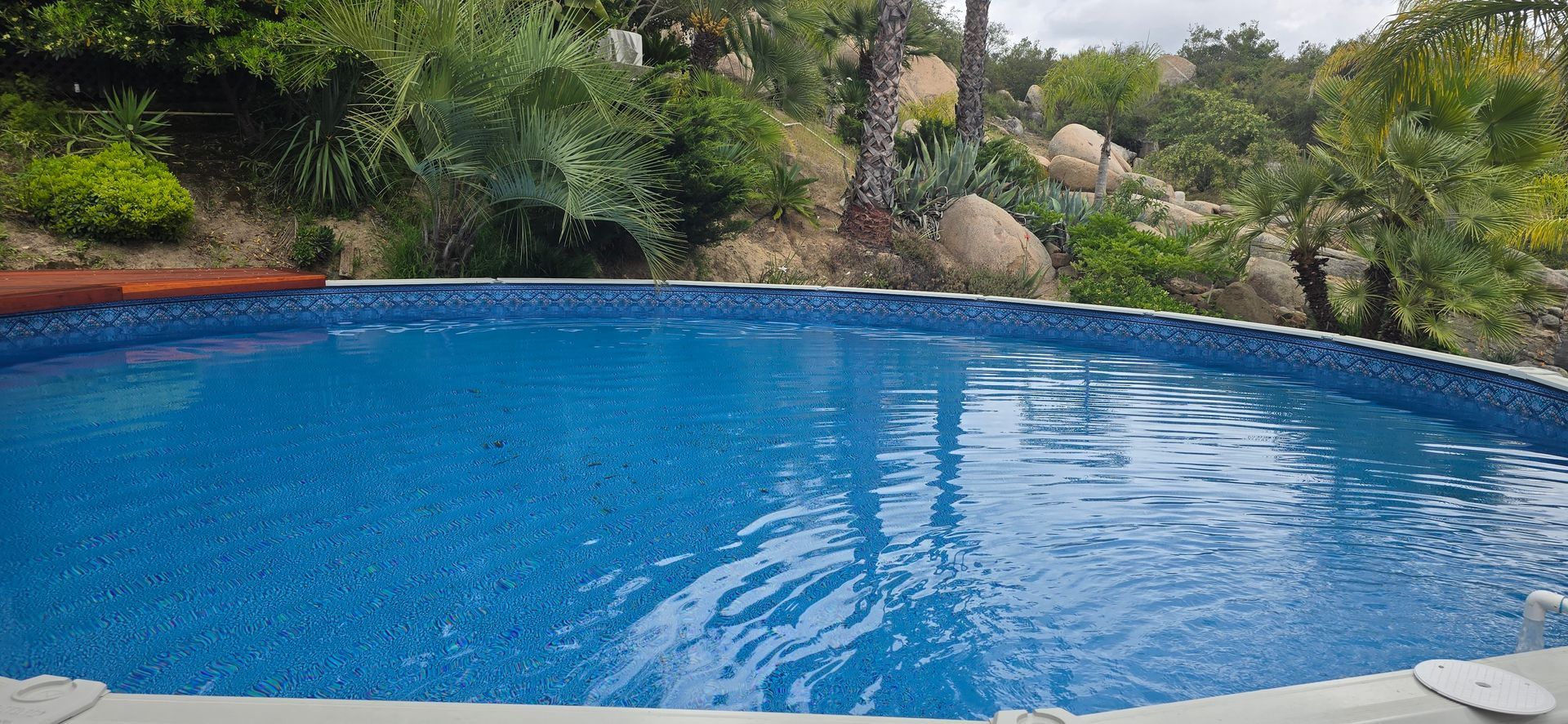 Blue swimming pool surrounded by rocks, greenery, and trees