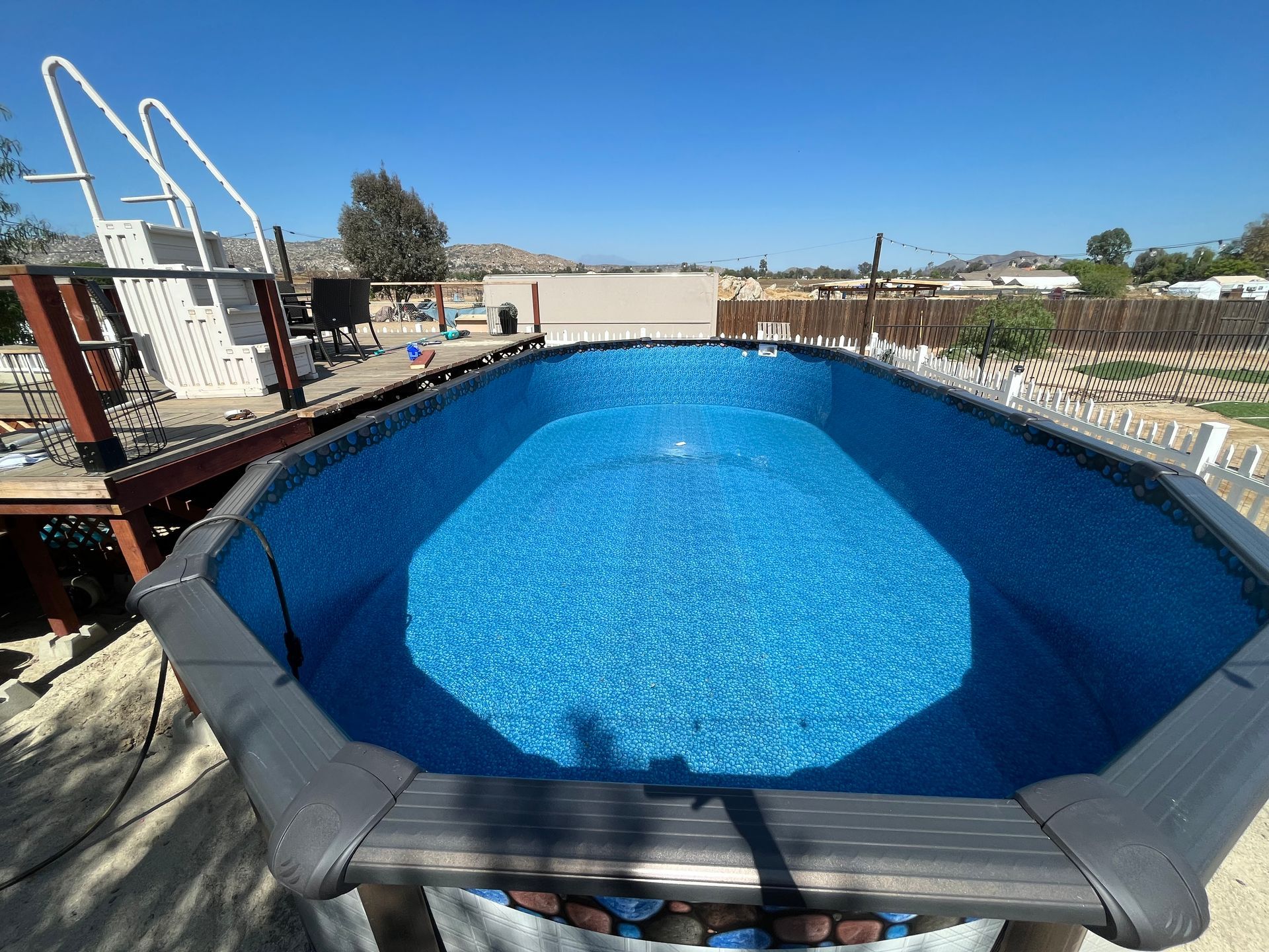 Above-ground pool filled with bright blue water in a backyard on a sunny day