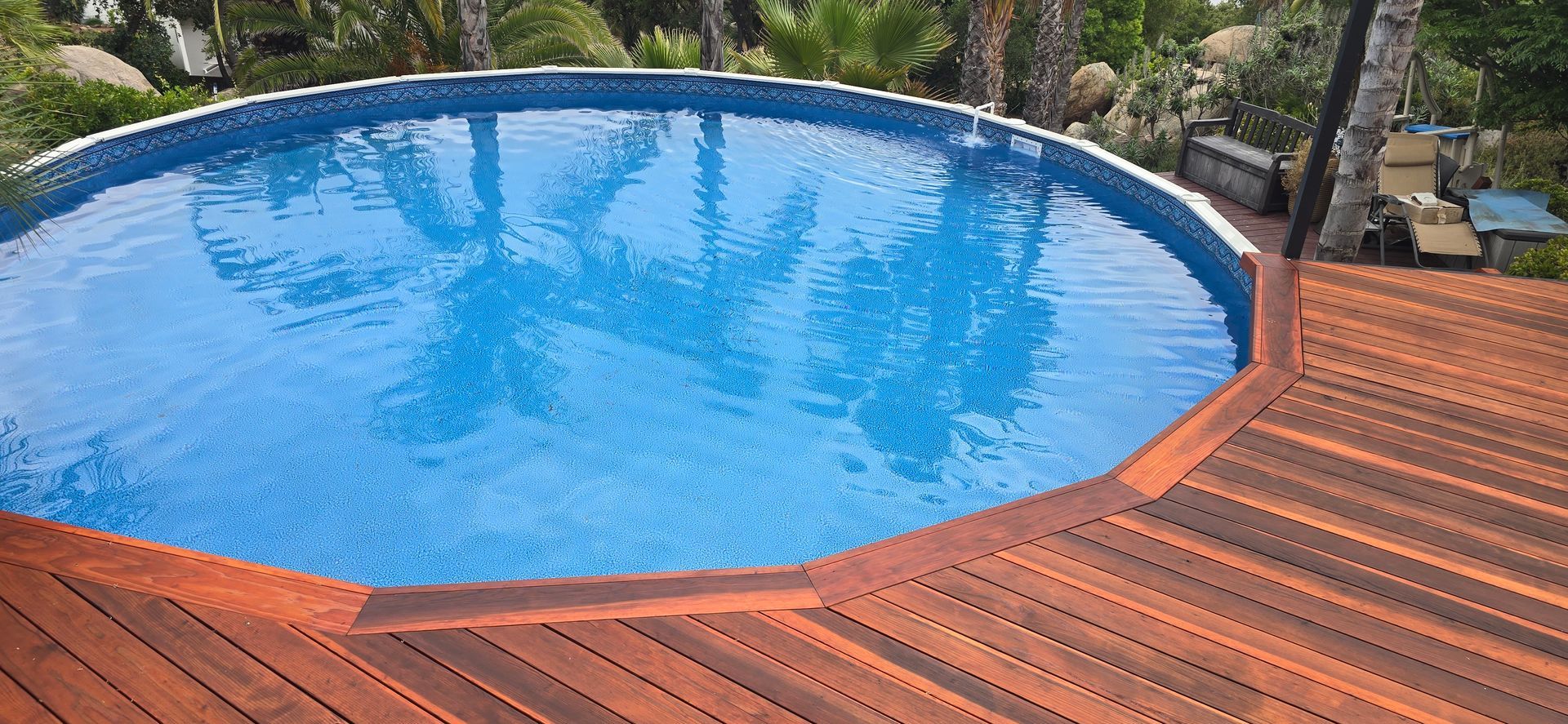 Backyard pool with clear blue water bordered by a curved wooden deck and rocks