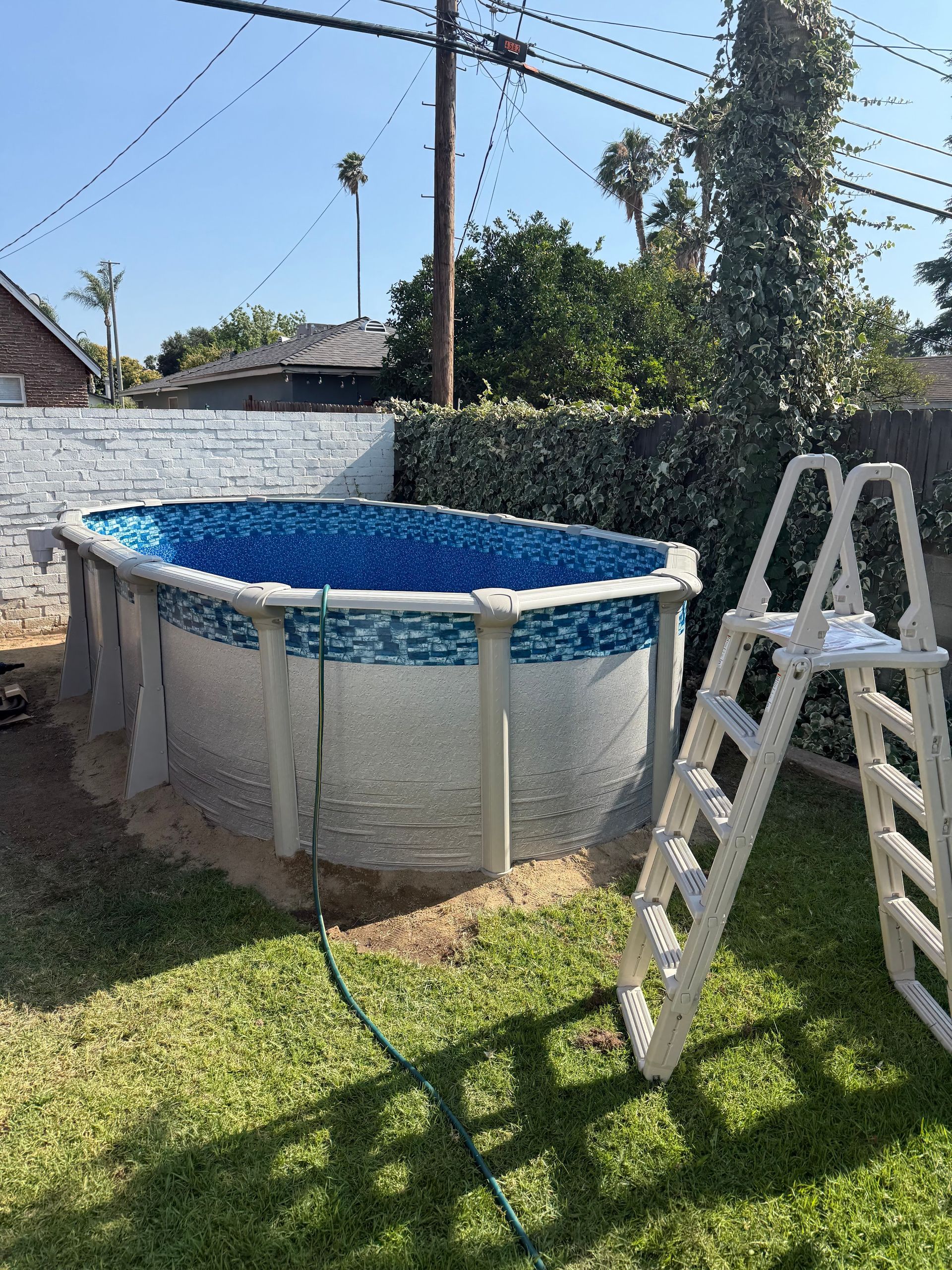 Above-ground pool in a backyard with a white ladder and blue liner in sunny weather