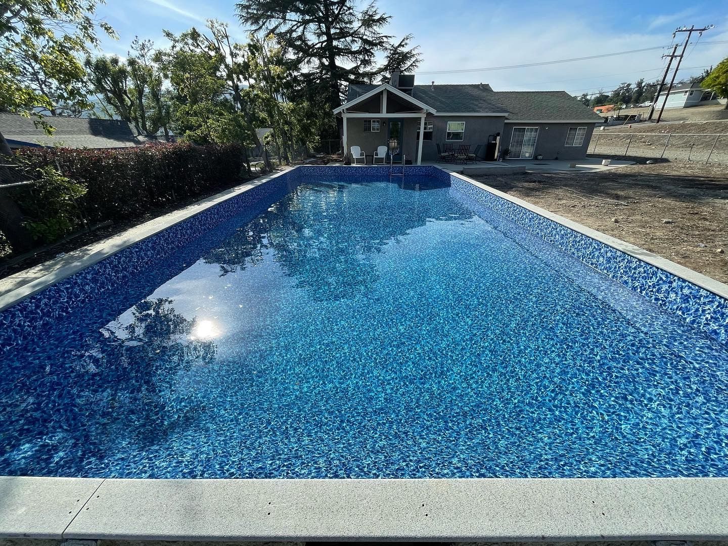 Blue swimming pool with sparkling water in a backyard, with a small building and trees behind it