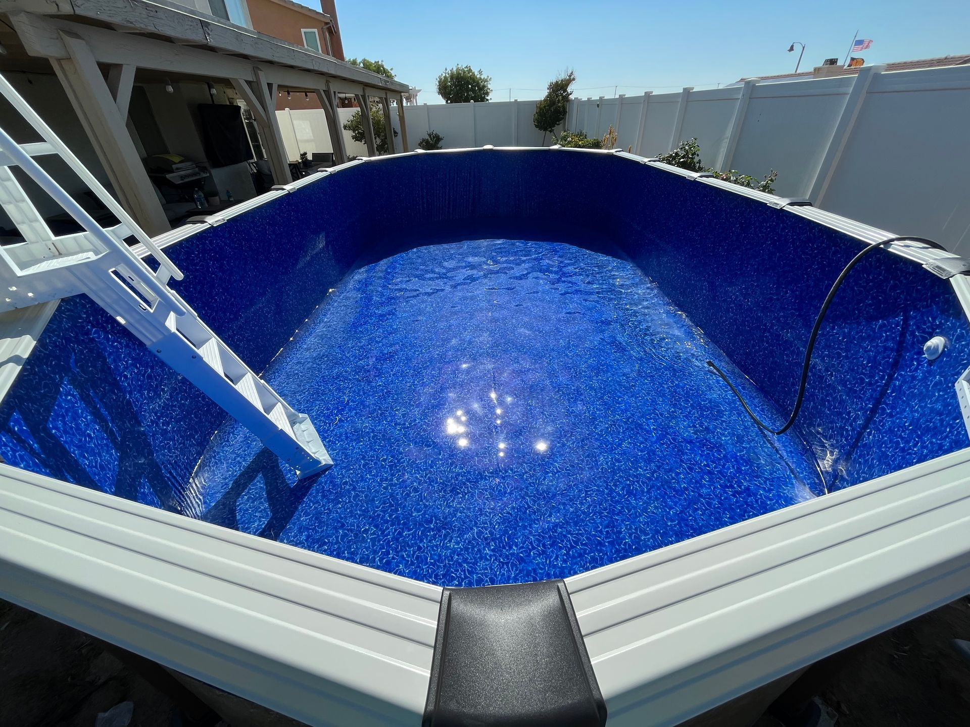 Empty blue swimming pool being lined, with a ladder and sunlight reflecting on the waterless surface