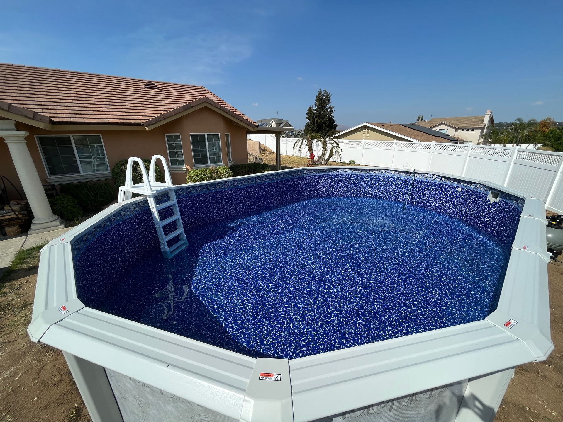 Above-ground pool with blue mosaic liner, white ladder, and desert backyard under a clear sky