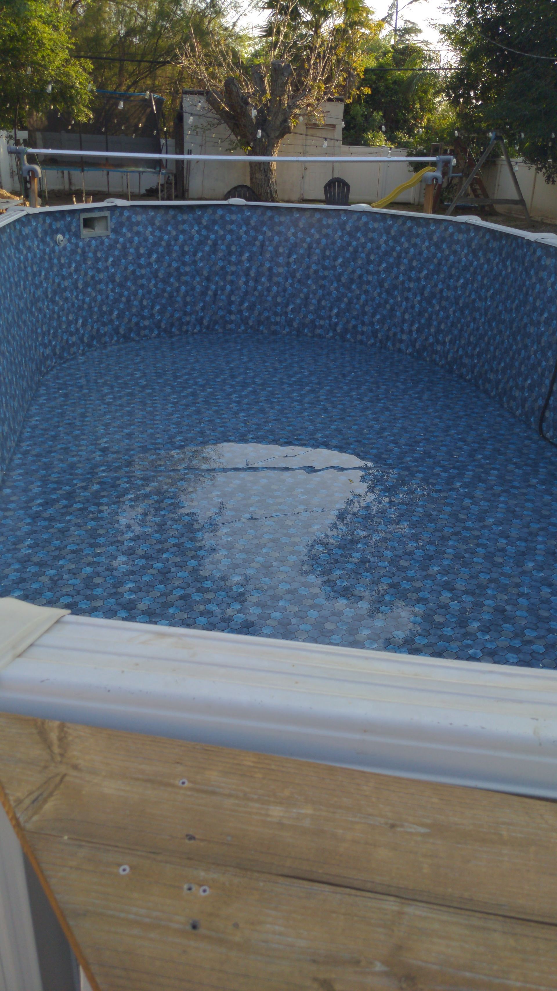 Empty blue-tiled swimming pool with a wooden exterior, seen outdoors in daylight