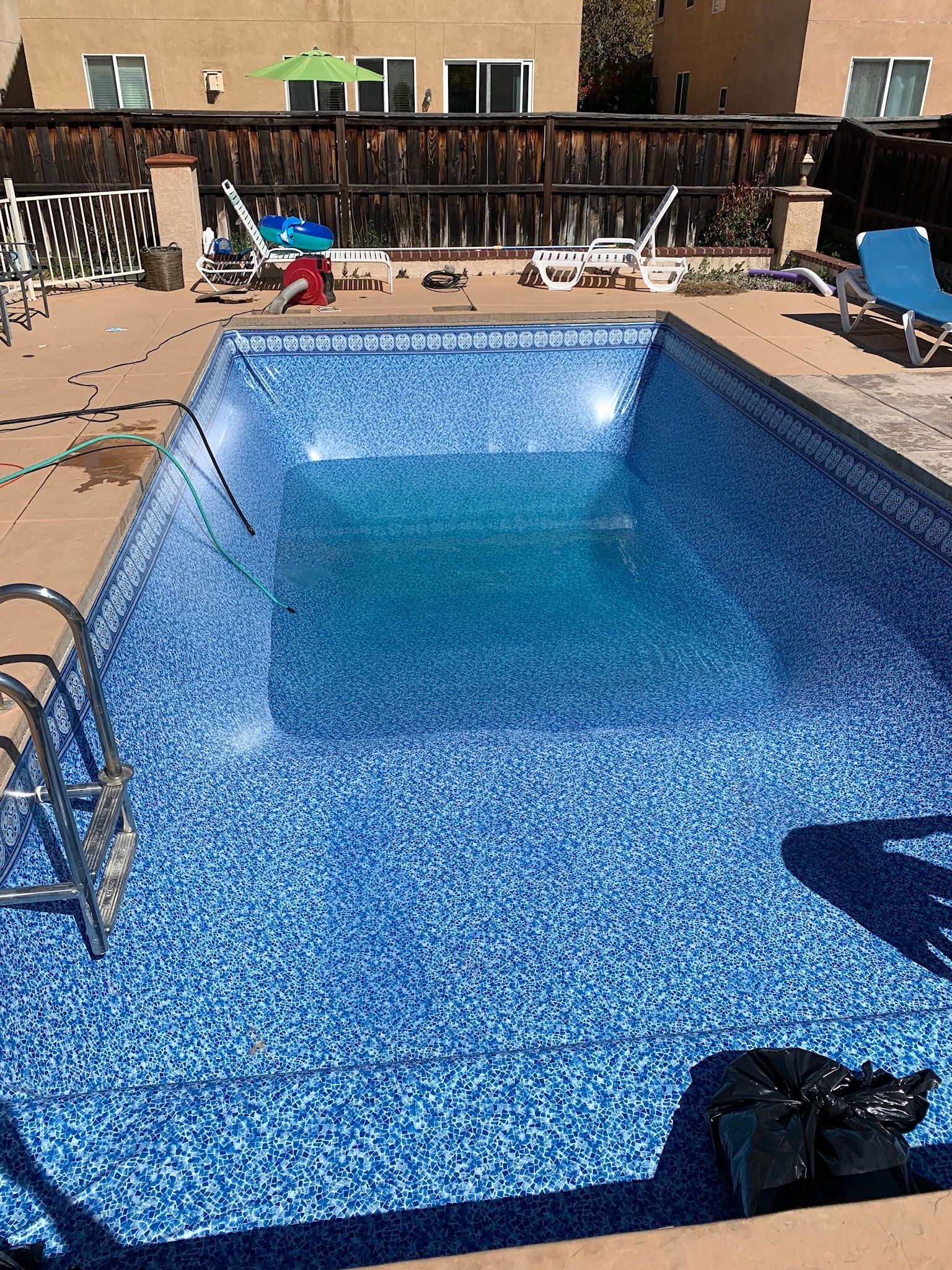 Backyard swimming pool with blue water, lounge chairs, and wooden fence in bright sunlight