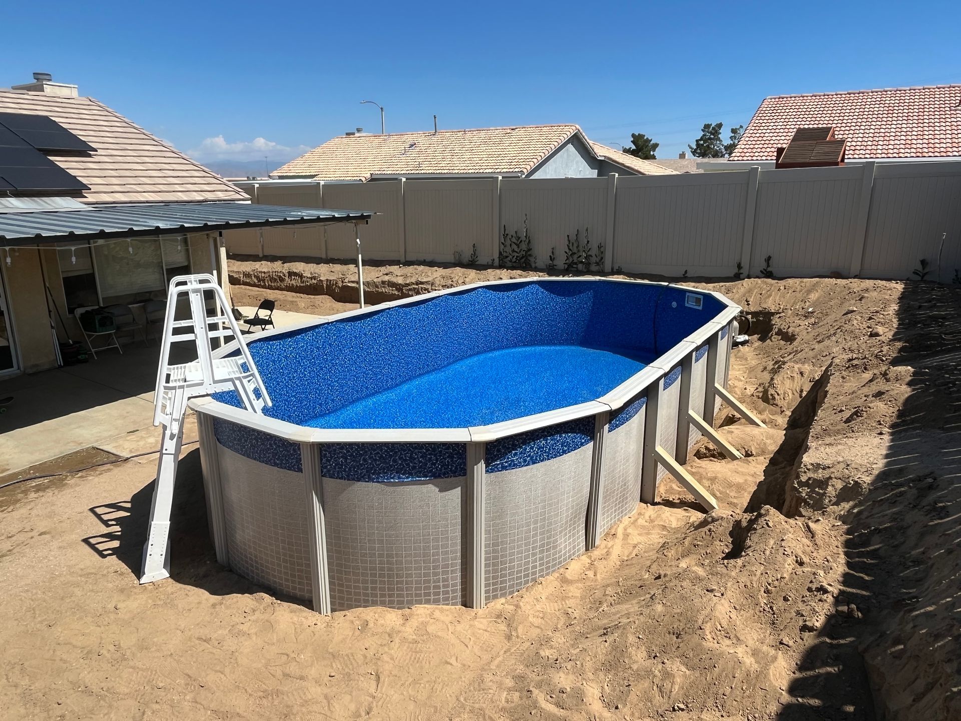 Above-ground pool being installed in a backyard, with a ladder and dirt surrounding it.