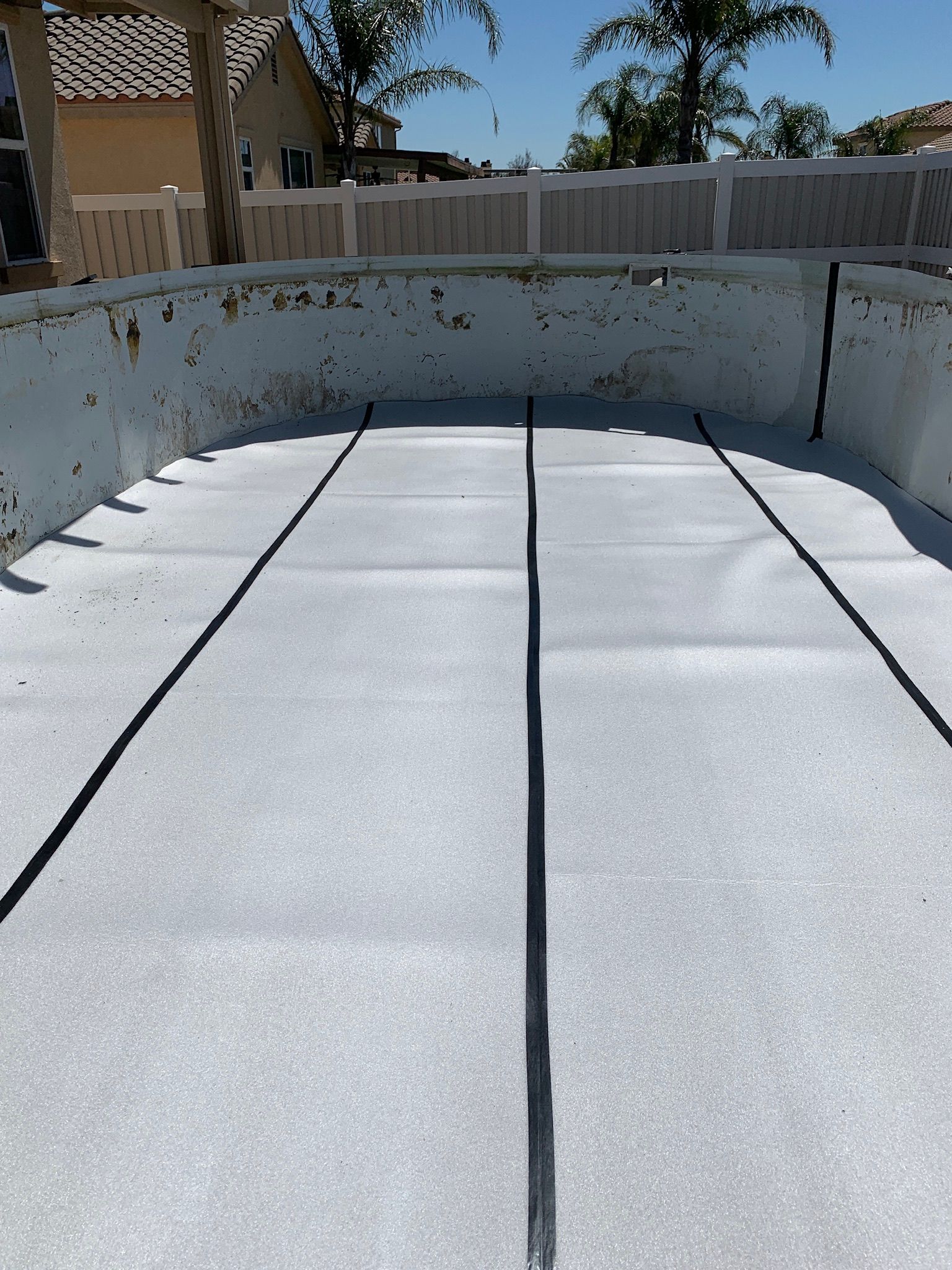 Empty above-ground pool with a white liner and blue top rail in a backyard