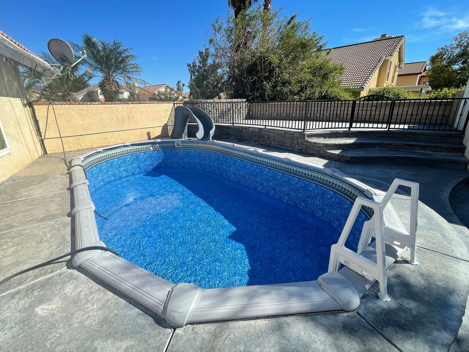 Backyard above-ground pool with blue water, safety cover, and ladder under a clear sky