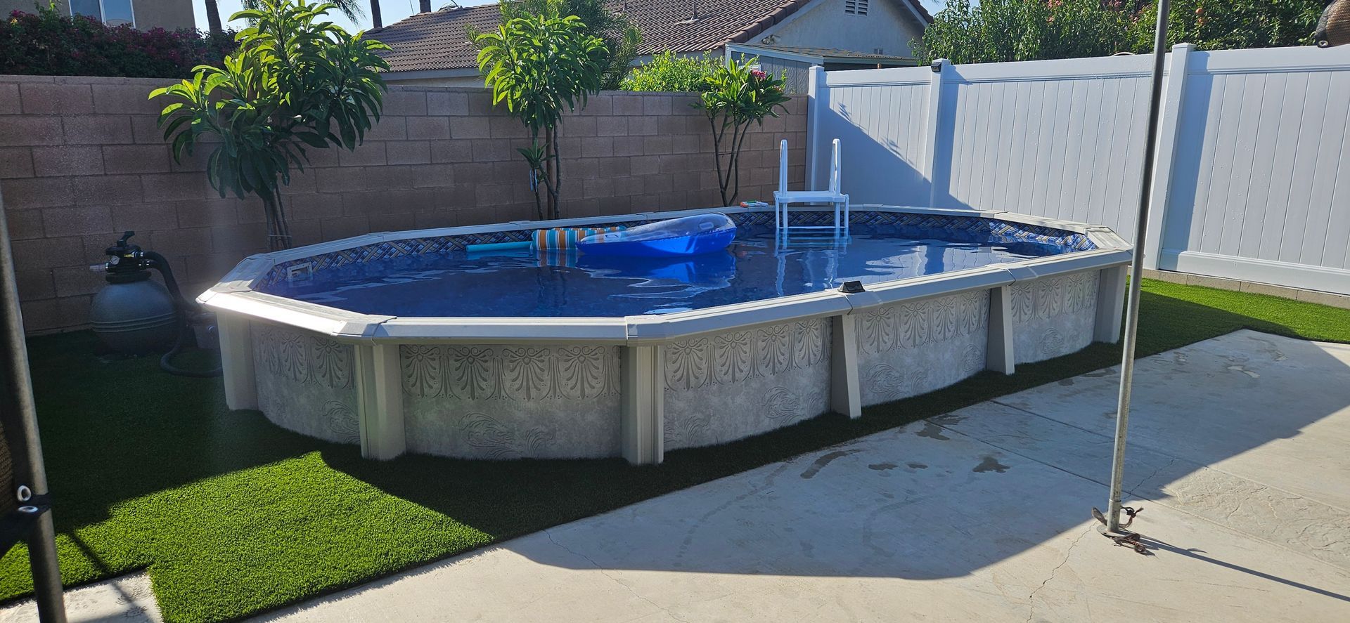 Above-ground pool with blue cover in a sunny backyard beside a concrete patio and small trees.