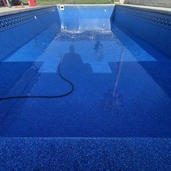 Empty blue swimming pool being cleaned, with a hose and water spraying at the far end