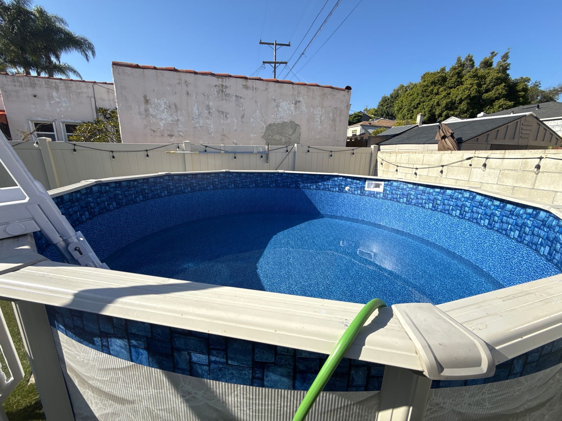 Empty above-ground pool with blue mosaic liner and beige deck in a backyard.