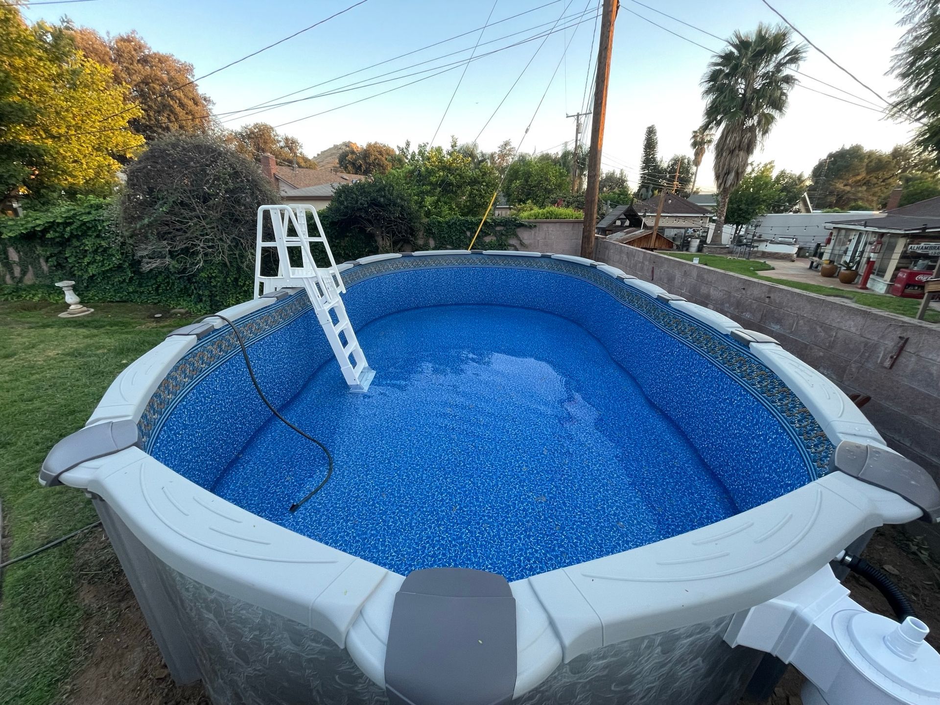 Empty above-ground pool with blue liner and white ladder in a backyard at dusk