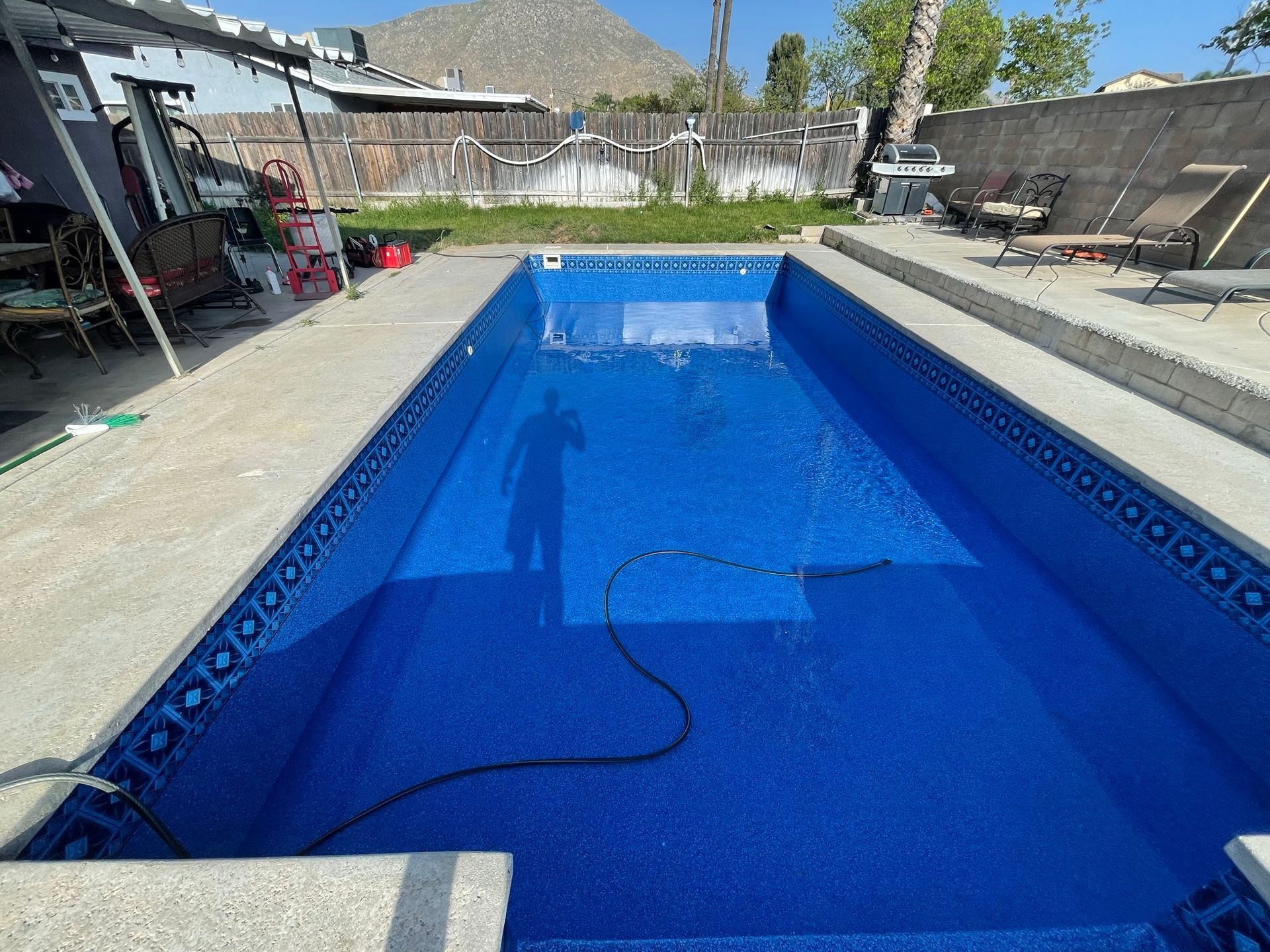 Empty blue swimming pool under construction in a backyard, with a hose in the water and unfinished surroundings