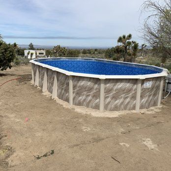 Above-ground pool with blue water in a dry yard overlooking a distant landscape