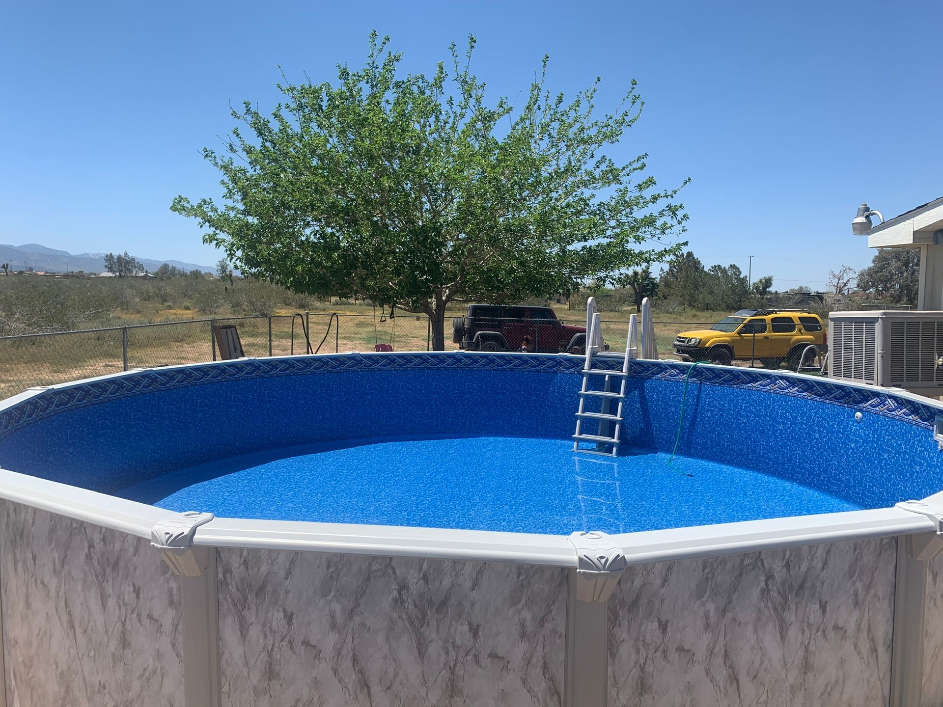 Round above-ground pool with blue water and a ladder in a sunny backyard