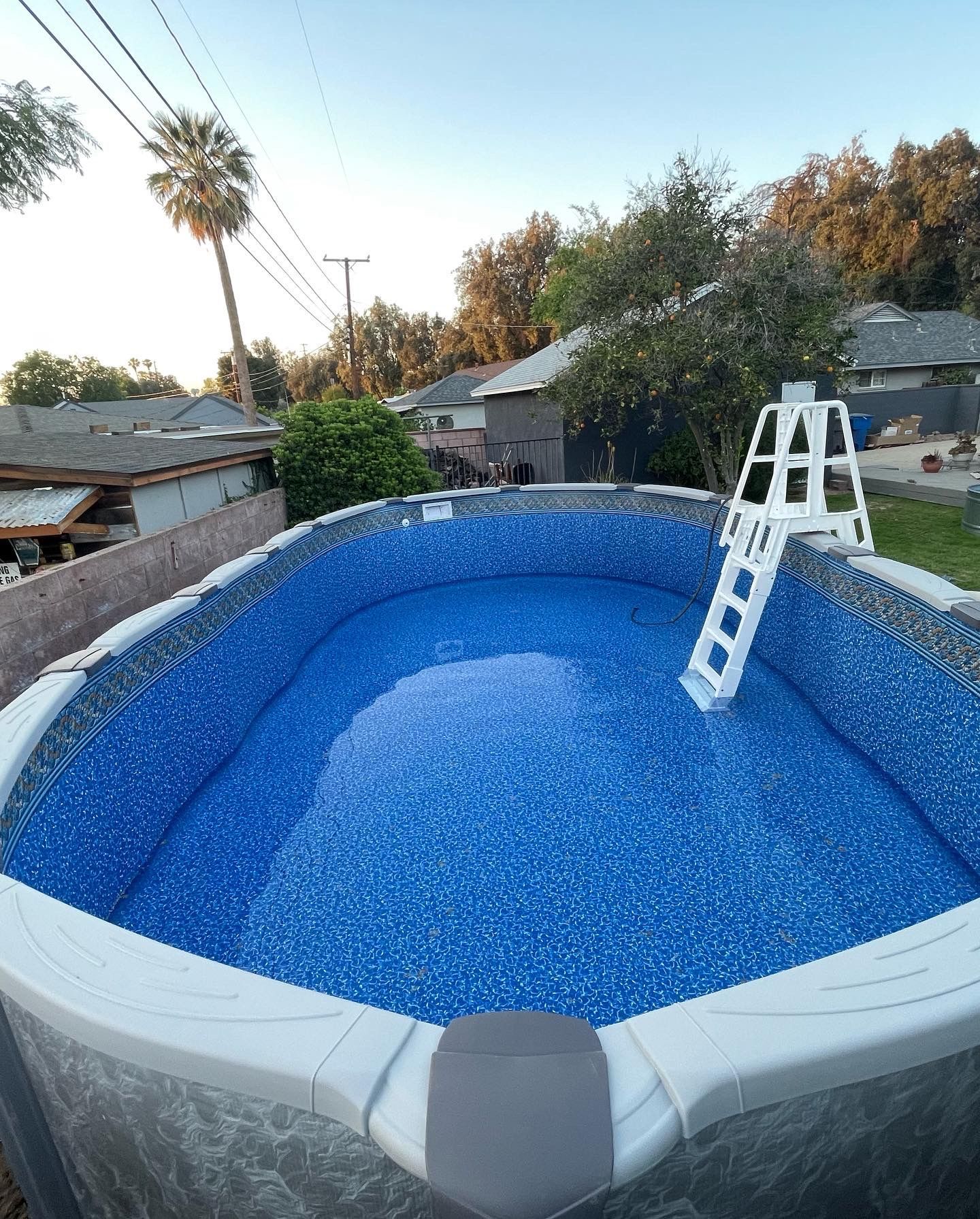 Above-ground pool with a blue liner and a white ladder in a backyard at sunset