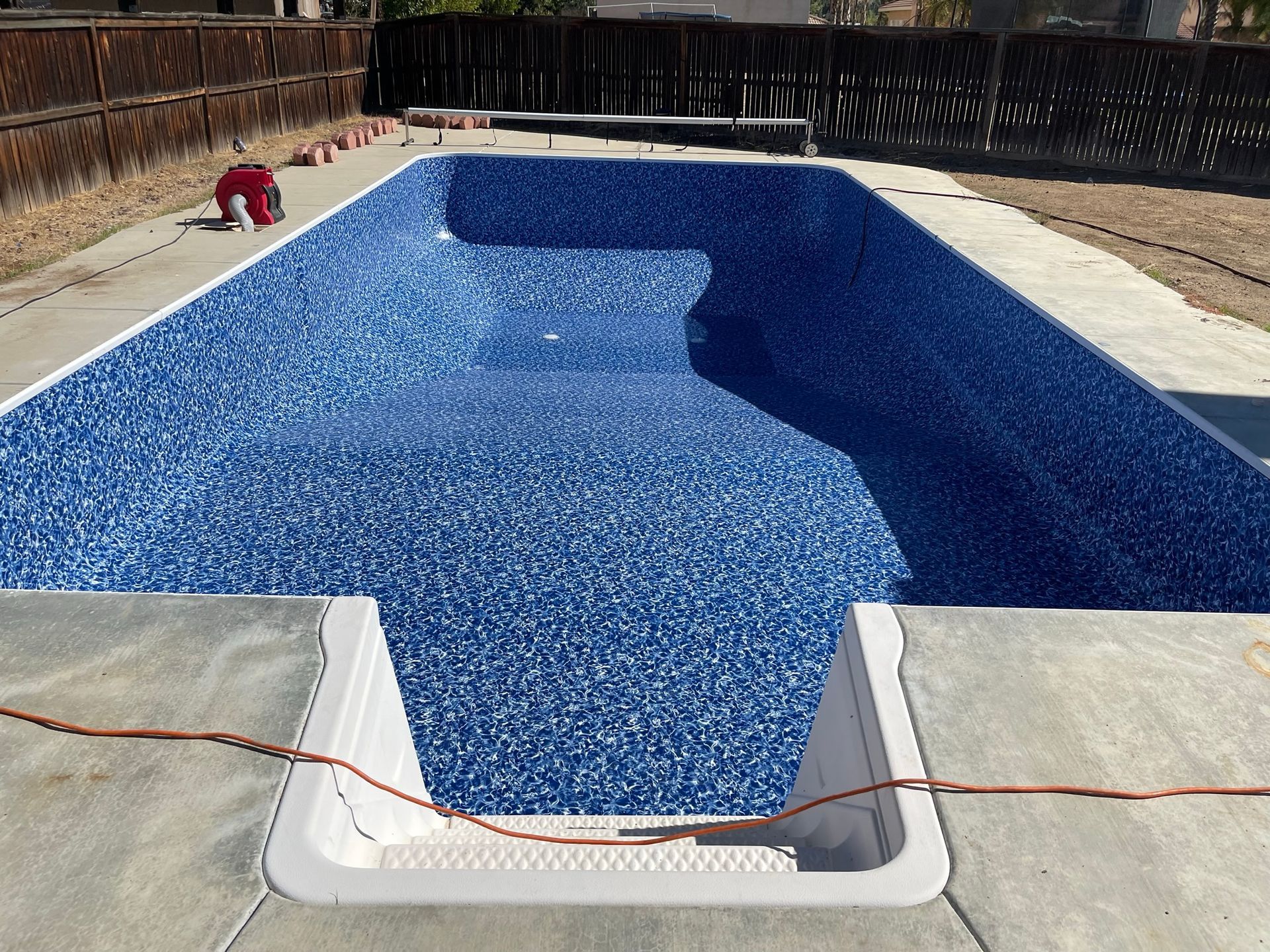 Empty blue swimming pool being resurfaced, with a worker on the left side.