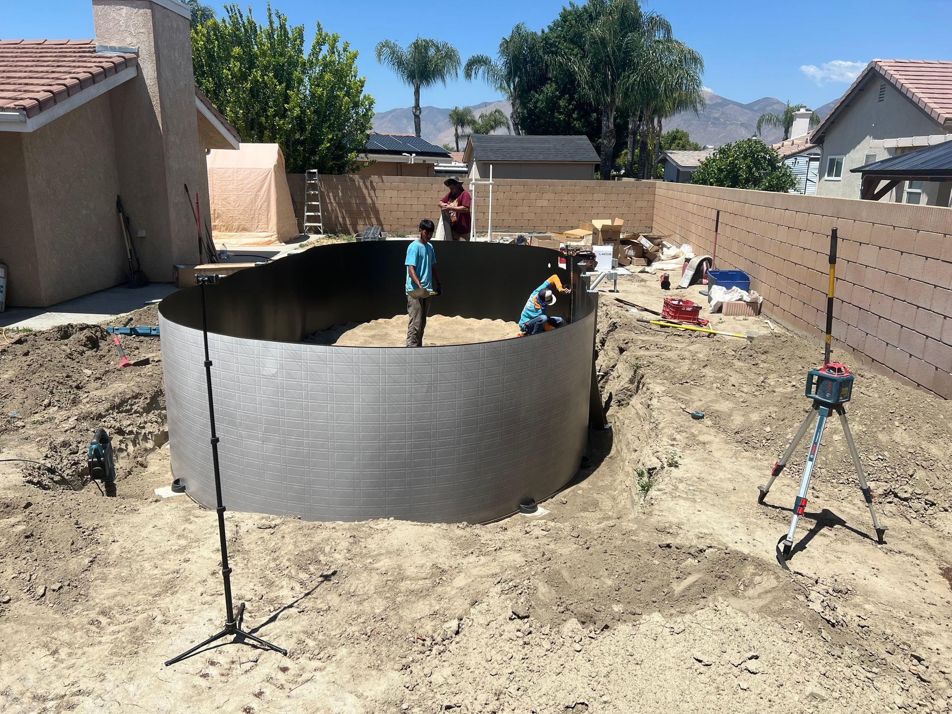 People working at a backyard construction site beside a round steel pool frame