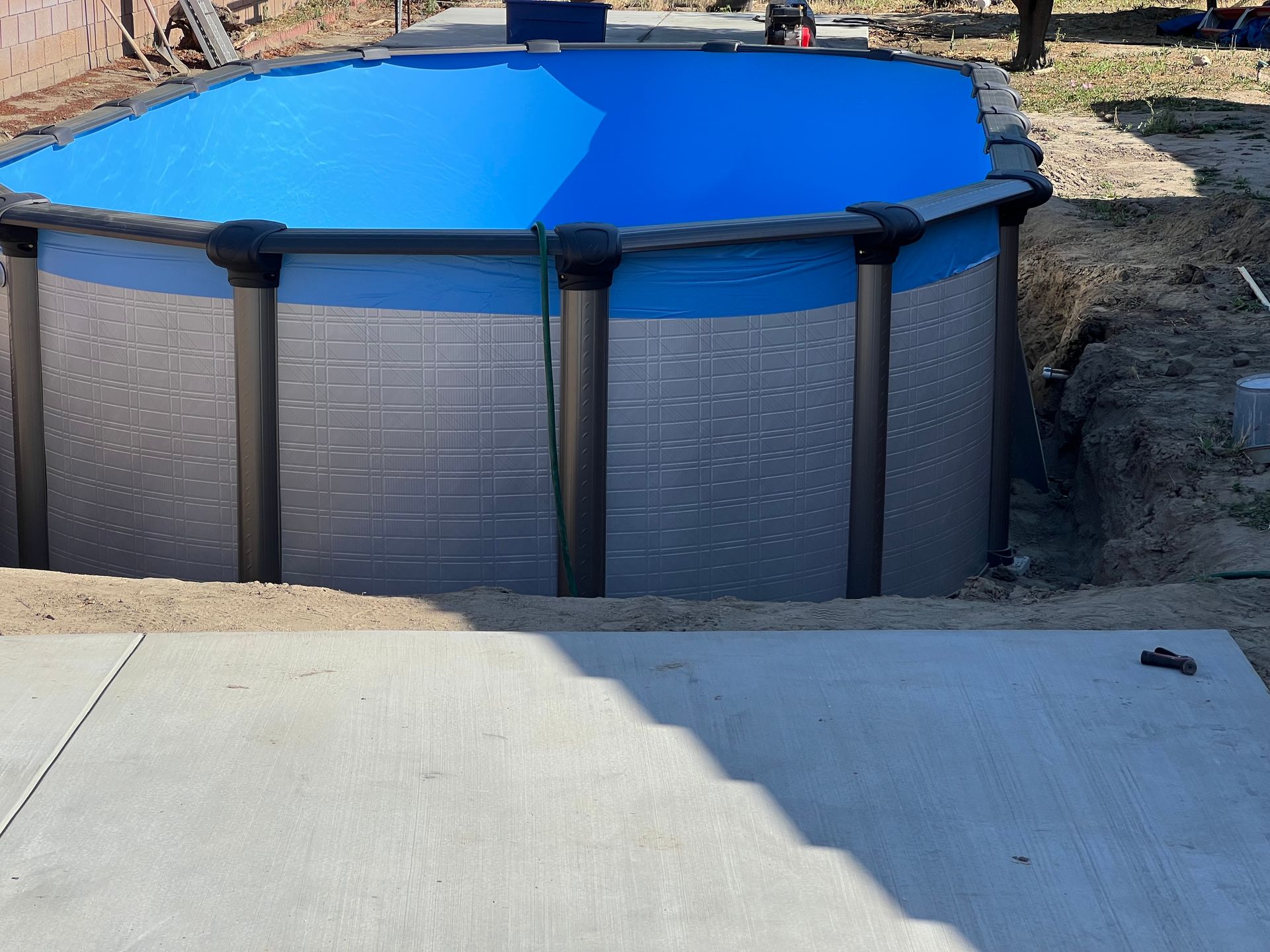 Above-ground pool with a bright blue cover in a backyard, beside a concrete patio