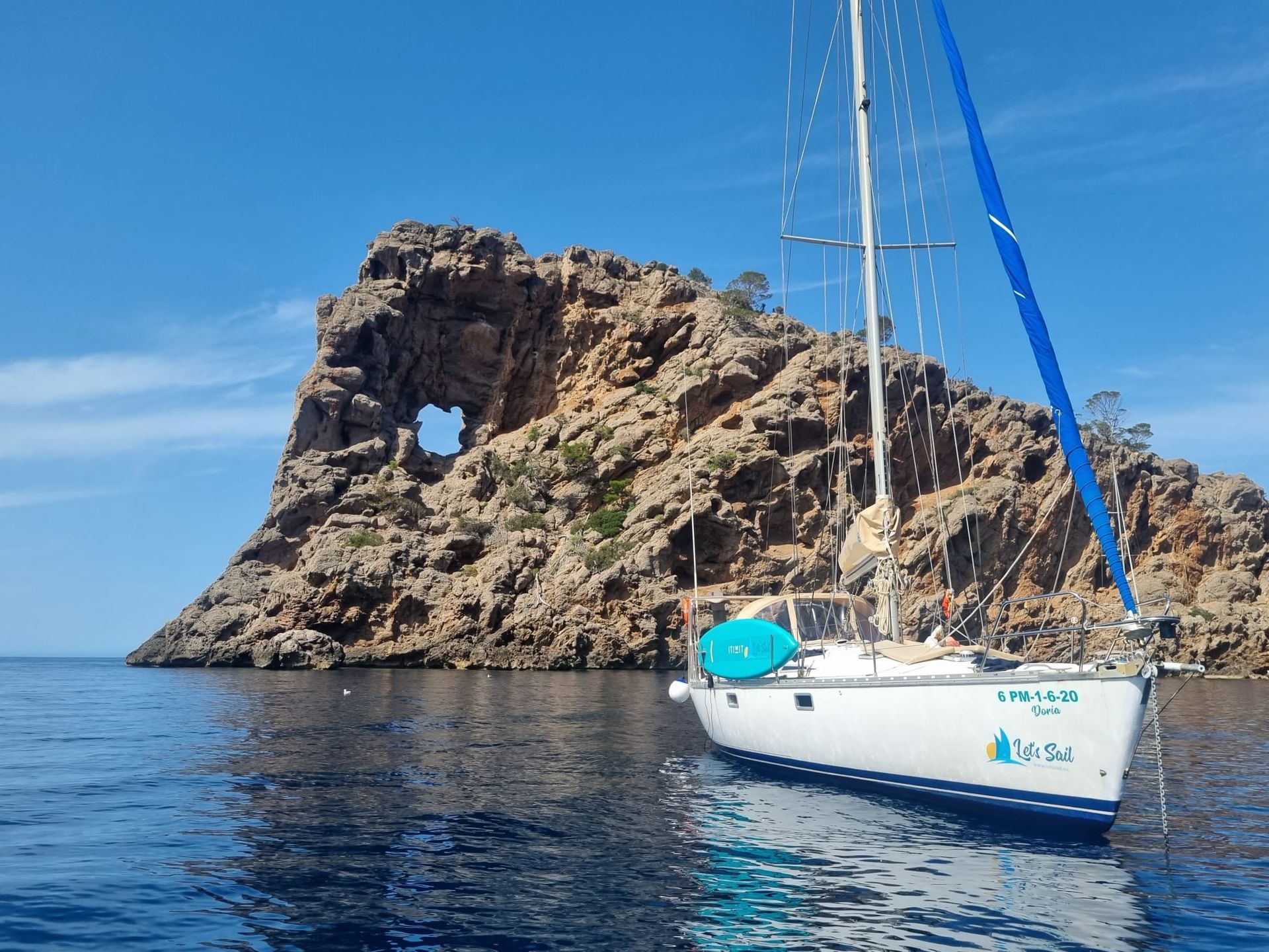 Un velero flota en el océano frente a una isla rocosa.